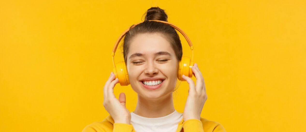 young woman wears headphones-yellow background