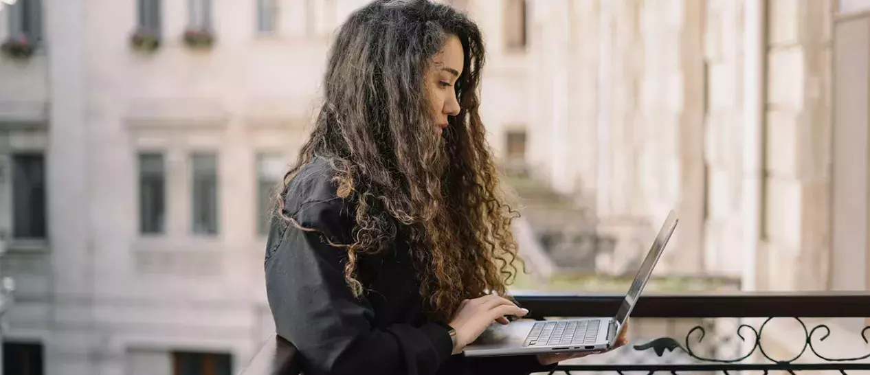 Μία γυναίκα χρησιμοποιεί το νέο της laptop που πήρε από τον ΓΕΡΜΑΝΟ τη Black Friday 2025 στο μπαλκόνι