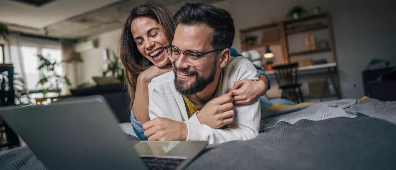 Ένα ζευγάρι γελάει στο κρεβάτι βλέποντας κάτι στο laptop