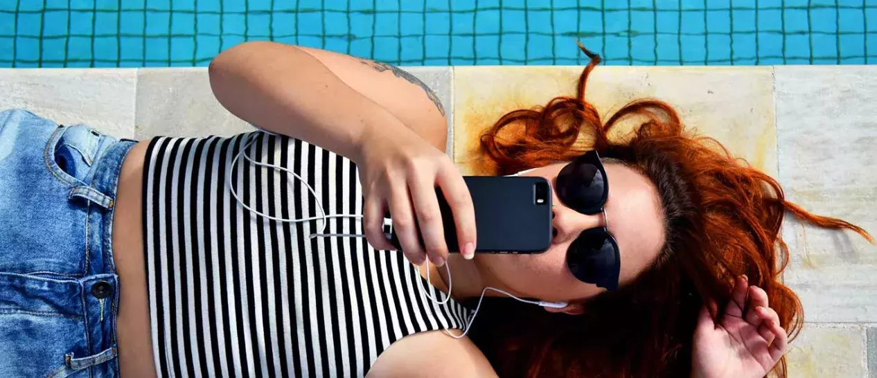 Μία κοπέλα χρησιμοποιεί το smartphone της στην άκρη της πισίνας
