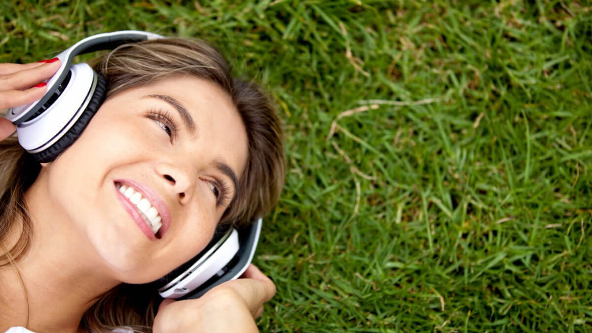 young woman wears headset lying on grass
