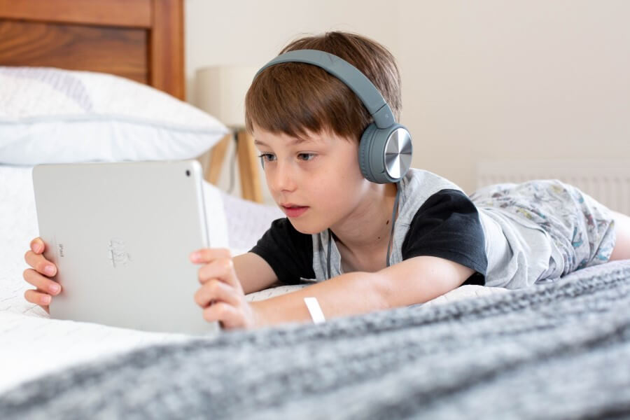 little boy lying in bed with tablet and headphones