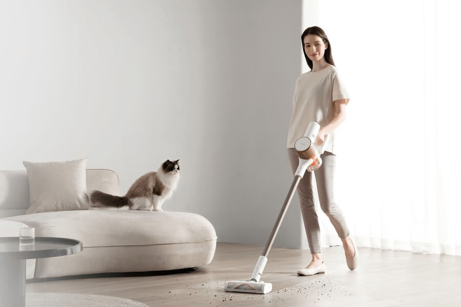 young woman using xiaomi stick vacuum cleaner and a cat watches her