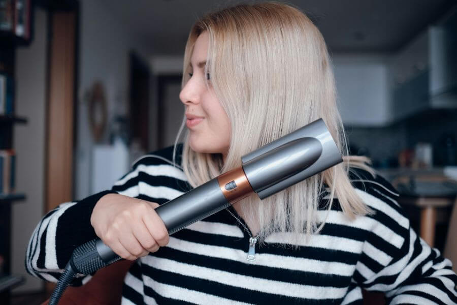 blonde woman uses hair straightener