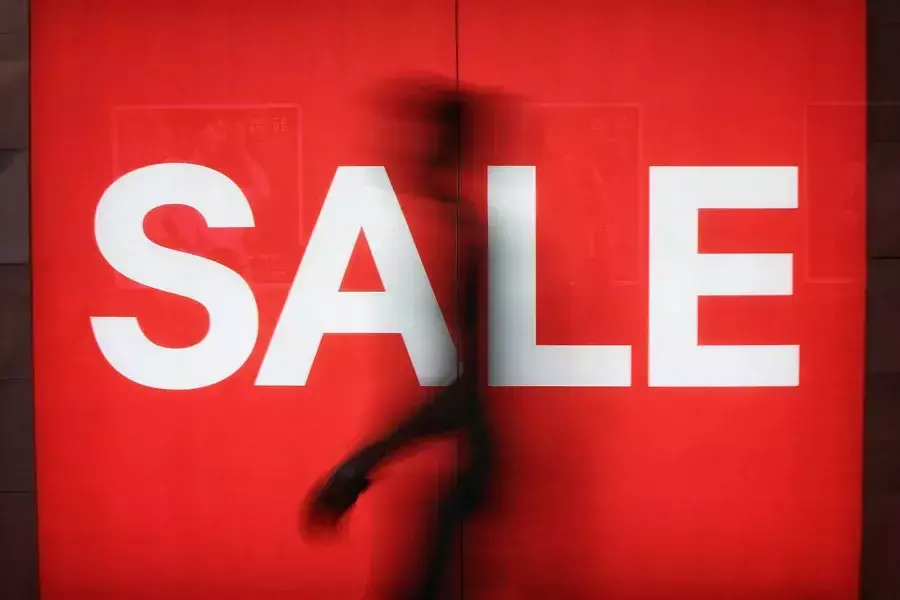 Μία ανθρώπινη σιλουέτα περπατά πίσω από μία βιτρίνα «ντυμένη» με την ένδειξη των εκπτώσεων