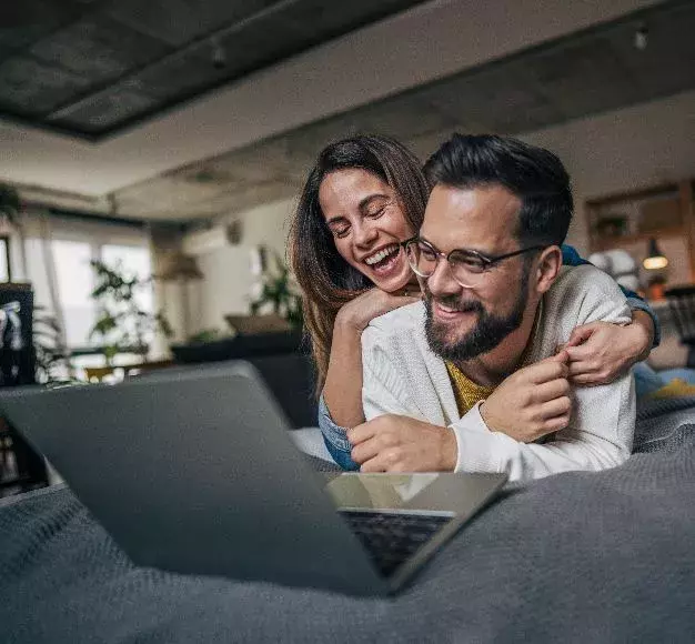 Ένα ζευγάρι γελάει στο κρεβάτι βλέποντας κάτι στο laptop