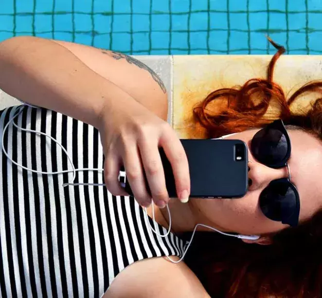 Μία κοπέλα χρησιμοποιεί το smartphone της στην άκρη της πισίνας